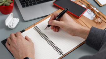 Man writing in agenda on a grey office desk close up. Business concept